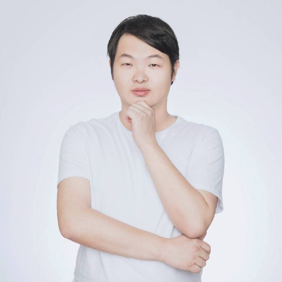 Person in a white shirt posing with one hand on chin against a light background.