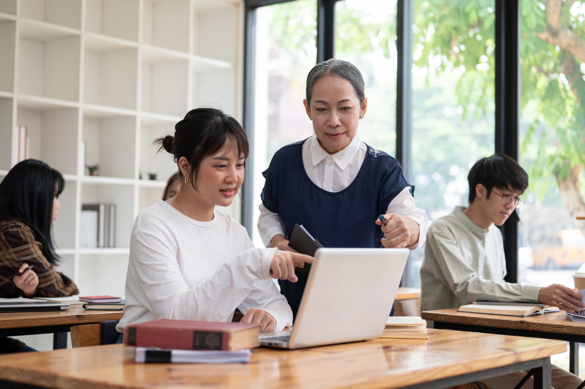 A mature Asian female teacher or professor helping and explaining a difficult question to a student.